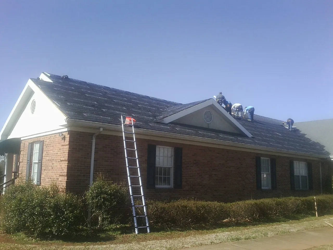 Crew tearing shingles off a brick ranch roof with a ladder set — Metal Roof Repair work by our crew in Convent Station