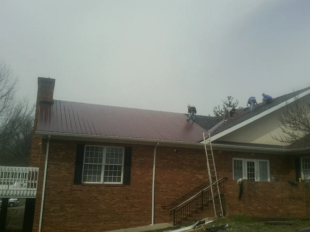 Crew setting red metal roofing panels on a brick home in Convent Station