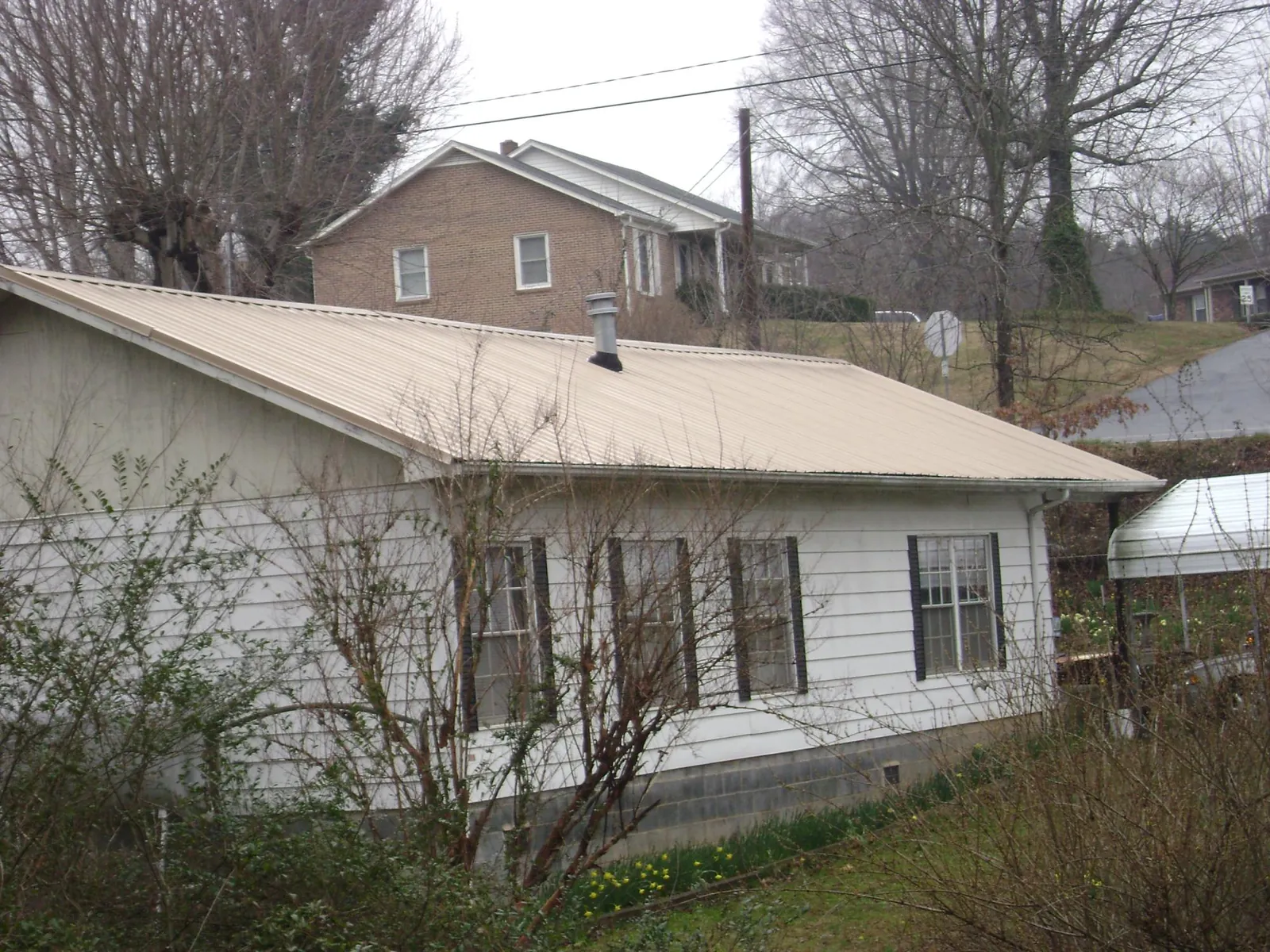 Tan metal roof on a white sided house set into a hillside — Commercial Roofing by Roofing Brothers in Convent Station